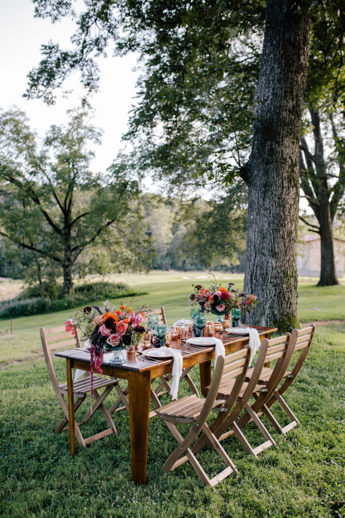 brown wooden dinner table with colorful flowers and white plates and gold silverware at Mill Creek Farm in Hiddenite NC.