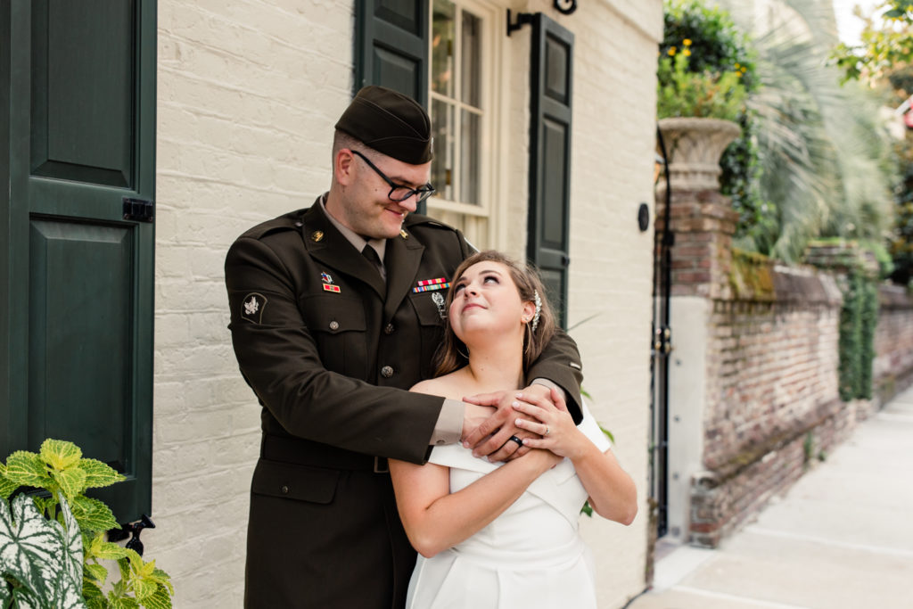 Groom, wearing military uniform, hugging his bride, in a white jump suit in Charleston.