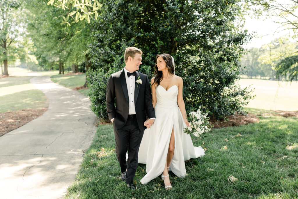 Bride, in white strapless gown, walking holding hands with groom, in black suit, at Long View Country Club Wedding Venue Charlotte NC