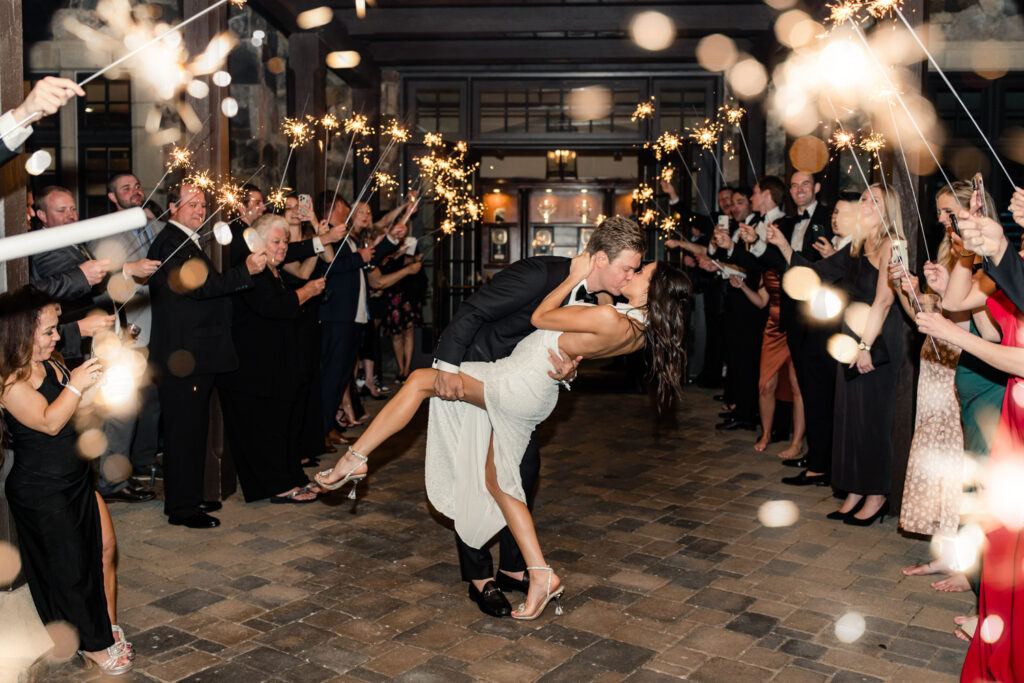 Bride, in white sparkle dress, kissing groom, in black suit, on the during sparkler exit at Long View Country Club Wedding Venue Charlotte NC