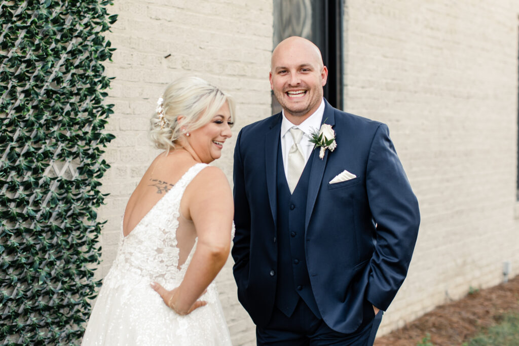 Bride with blonde hair in a white lace dress seeing her groom, in a navy suit for the first time at The Bottle Factory Wedding Venue. Photographed by Charlotte wedding photographer.