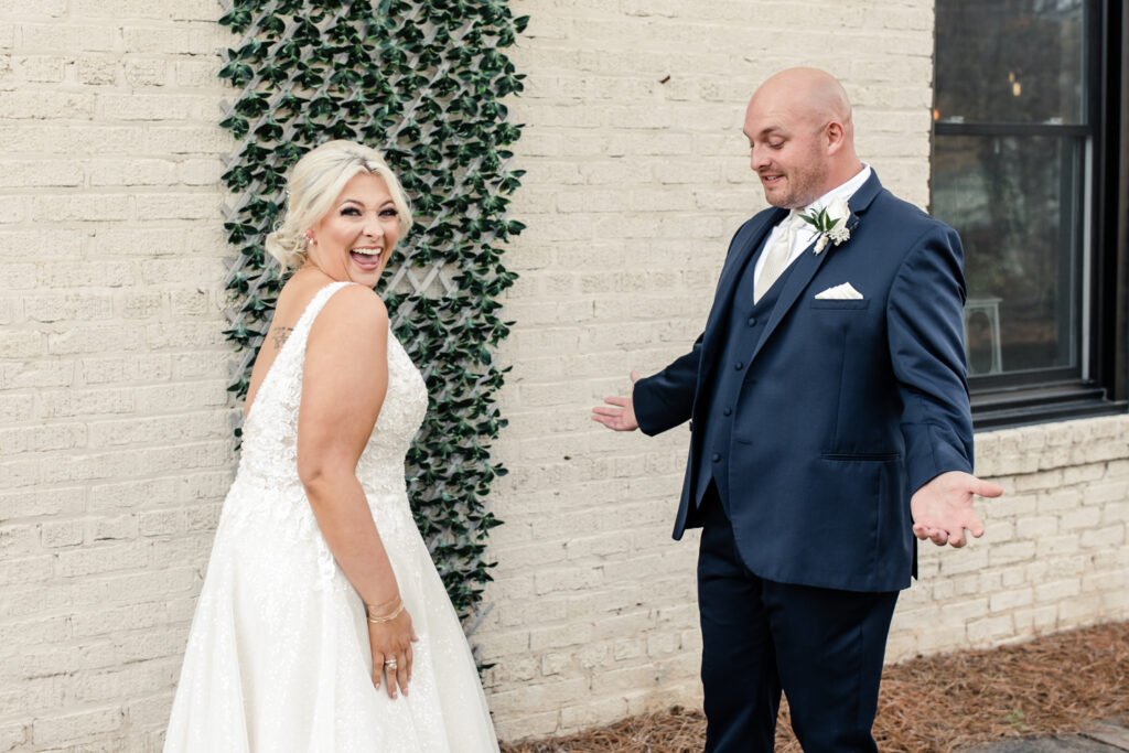 Bride with blonde hair in a white lace dress seeing her groom, in a navy suit for the first time at The Bottle Factory Wedding Venue. Photographed by Charlotte wedding photographer.