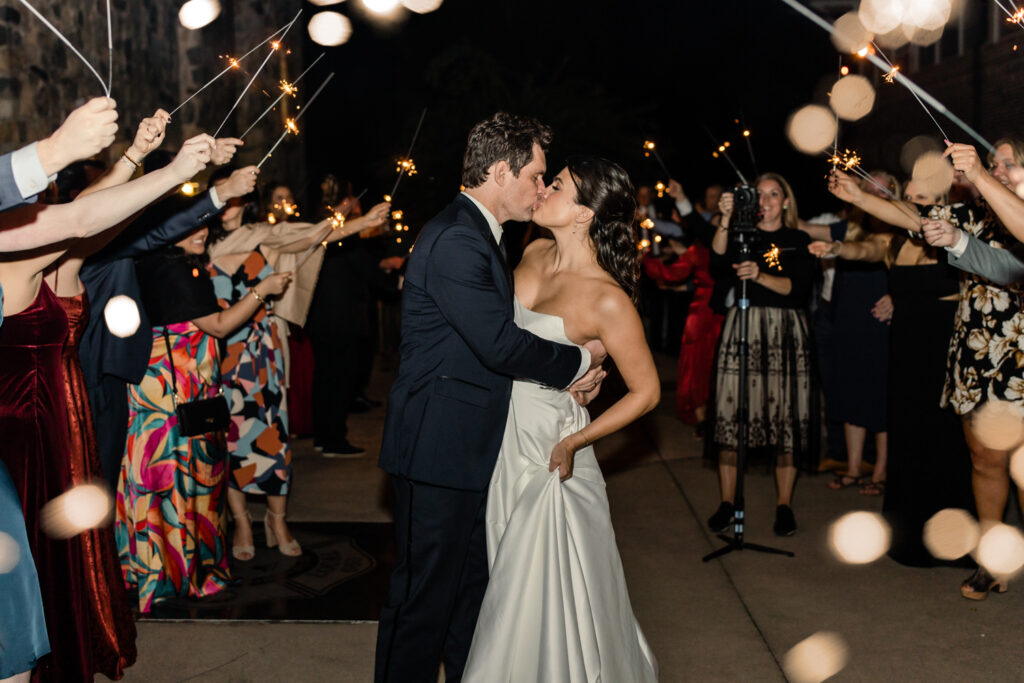 Bride with brown hair in a white strapless dress kissing groom with brown hair in a navy suit under under sparklers at The Palmer Building Wedding Venue. Photographed by Charlotte Wedding photographer, Stephanie Bailey.