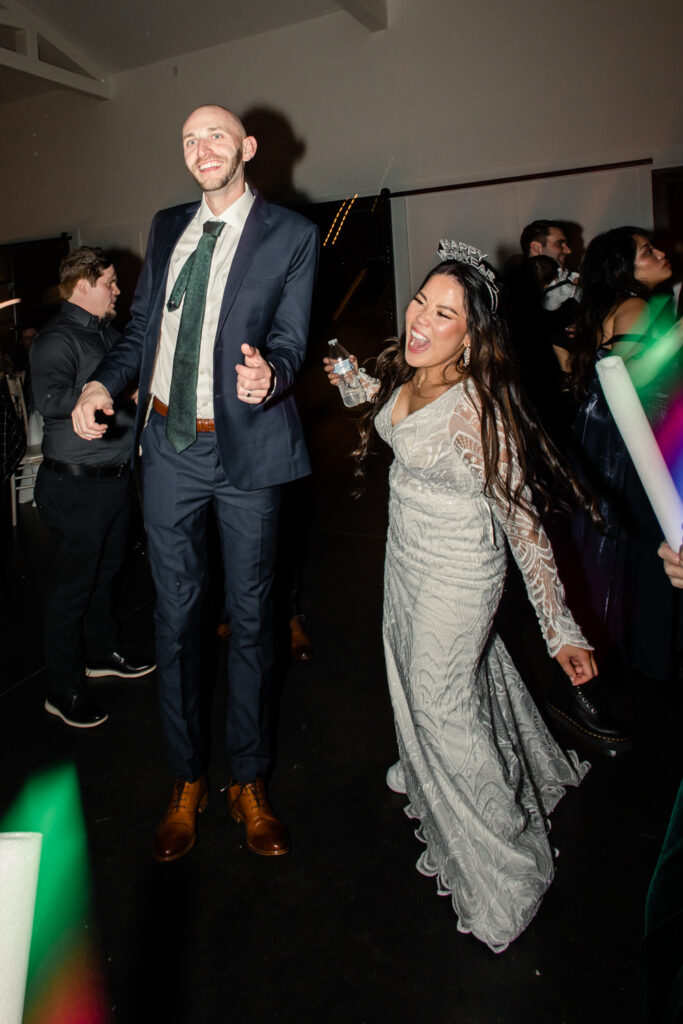 Bride with dark brown hair in a long white lace dress dancing with groom in navy suit and green tie during reception at Fields at Skycrest Wedding Venue in Charlotte NC. Photographed by Charlotte wedding photographer.